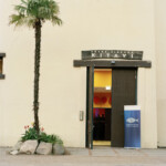 Eventeingang »Kitavi«, Hagenbecks Tierpark 2022.
Die Familie Hagenbeck stellte ab 1875 Menschen aus den Kolonien in sogenannten Völkerschauen zur Besichtigung aus. In diesen wurden Menschen z.B. aus Somalia, Kamerun oder Asien in ihnen zugeschrieben Tänzen und alltäglichen Verrichtungen präsentiert. Hagenbeck’sche Ausstellungen sollten Menschen und Tiere in scheinbar authentischen Umgebungen präsentieren. Hagenbeck warb für seine Völkerschauen unter anderem auf den Weltausstellungen in Chicago (1893) und in St. Louis (1904). Hagenbecks Tierpark